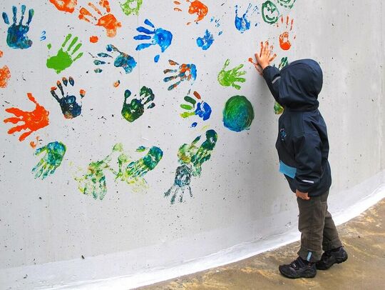 Enfant qui met en peinture sur un mur blanc avec ses mains